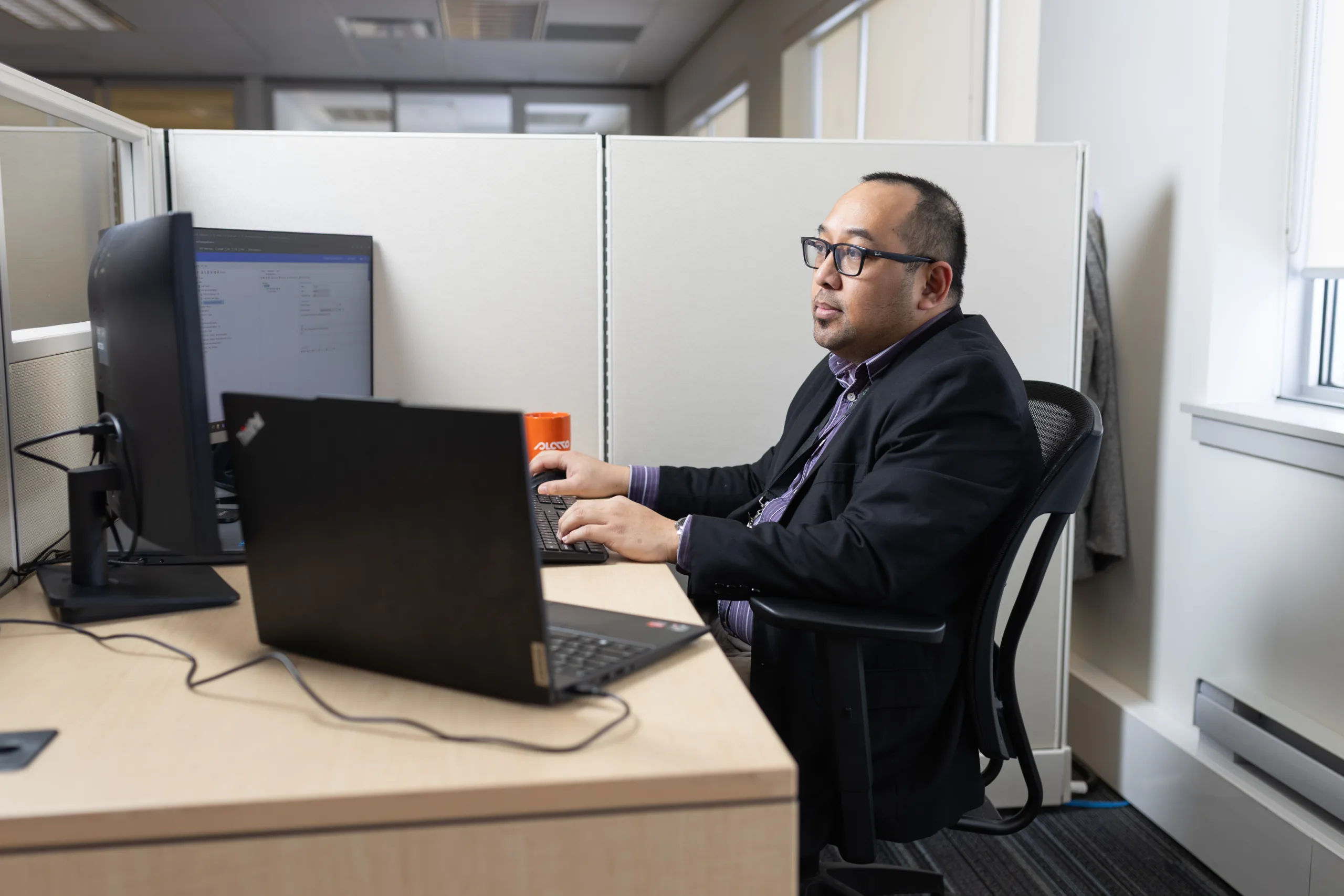 Side view of a man sitting at a desk, looking at a computer screen.